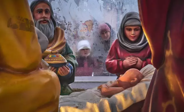 FILE - People look through a frosted plastic tent into a Christmas crib installed near Kazansky Cathedral during Orthodox Christmas celebrations in St. Petersburg, Russia, Wednesday, Jan. 7, 2026. (AP Photo/Dmitri Lovetsky, File)