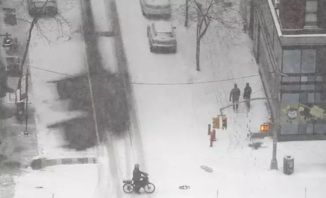 Pedestrians walk and ride their bike as heavy snow falls, Sunday, Jan. 25, 2026, in New York. (AP Photo/Heather Khalifa)