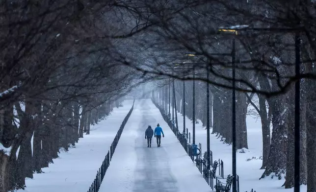 Two people walk along the National Mall as snow falls, Sunday, Jan. 25, 2026, in Washington. (AP Photo/Alex Brandon)