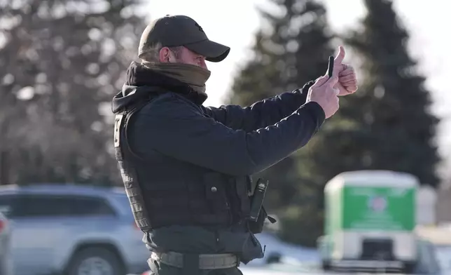 A federal immigration officer films cars around him as people honk and whistle Tuesday, Jan. 20, 2026, in Roseville, Minn. (AP Photo/Angelina Katsanis)