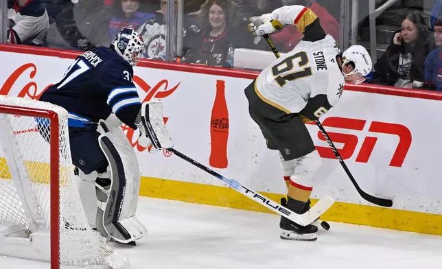Vegas Golden Knights' Mark Stone (61) and Winnipeg Jets goaltender Connor Hellebuyck (37) attempt to control a loose puck behind the net during the third period of their NHL hockey game in Winnipeg, Tuesday Jan. 6, 2026. (Fred Greenslade/The Canadian Press via AP)