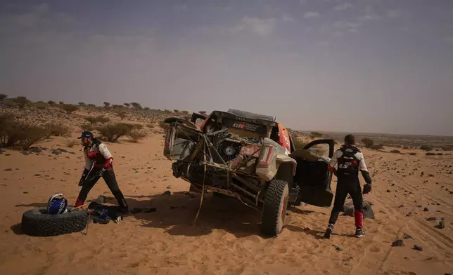 Driver Henk Lategan, left, and co-driver Brett Cummings repair their car during the eleventh stage of the Dakar Rally between Bisha and Al Henakiyah, Saudi Arabia, Thursday, Jan.15, 2026. (AP Photo/Thibault Camus)