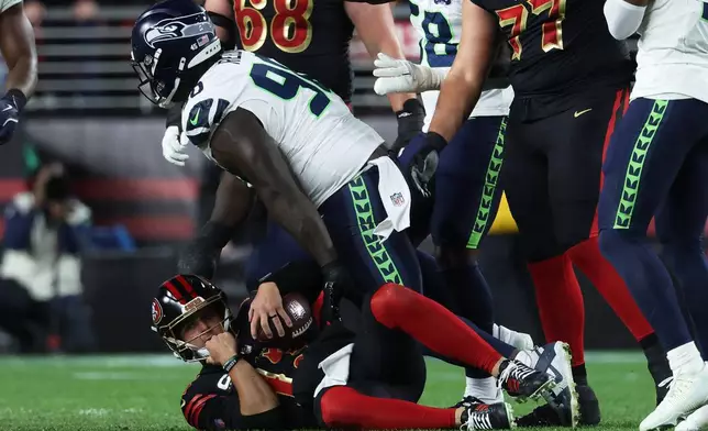 San Francisco 49ers quarterback Brock Purdy, bottom, reacts after being sacked by Seattle Seahawks defensive tackle Jarran Reed, middle, during the second half of an NFL football game in Santa Clara, Calif., Saturday, Jan. 3, 2026. (AP Photo/Jed Jacobsohn)