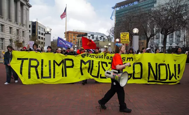 Protestors hold a banner stating "Trump Must Go Now" as they gather outside the UN Plaza during a demonstration against the U.S. bombing of Venezuela and seizure of Venezuelan President Nicolás Maduro, in San Francisco on Saturday, Jan. 3, 2026. (Yalonda M. James/San Francisco Chronicle via AP)