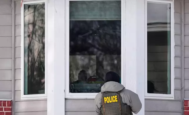 A federal immigration officer looks through a window of a home Tuesday, Jan. 20, 2026, in Maplewood, Minn. (AP Photo/Yuki Iwamura)