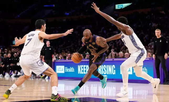Los Angeles Lakers forward LeBron James, center, drives toward the basket as Memphis Grizzlies forward Santi Aldama, left, and forward Jaren Jackson Jr. defend during the second half of an NBA basketball game Friday, Jan. 2, 2026, in Los Angeles. (AP Photo/Mark J. Terrill)