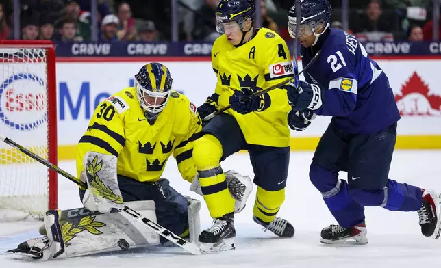 Sweden goalie Love Harenstam, left, defends the net as defenseman Leo Sahlin Wallenius, middle, and Finland forward Max Westergard compete for the puck during the first period of an IIHF World Junior Hockey Championship semifinals game, Sunday, Jan. 4, 2026, in St. Paul, Minn. (AP Photo/Matt Krohn)