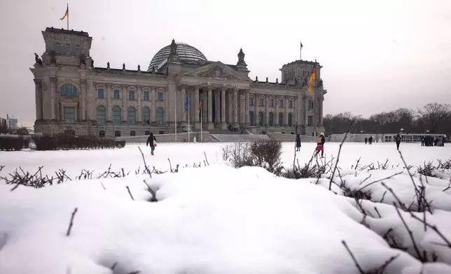 People walk in front of the Reichstag Building, home of the German parliament Bundestag, on a snowy winter day in Berlin, Germany, Thursday, Jan. 8, 2026. (AP Photo/Markus Schreiber)