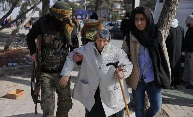 A Syrian government soldier helps an old woman who is fleeing from Sheikh Maqsoud and Achrafieh neighborhoods after clashes broke out on Tuesday between Syrian government forces and Kurdish fighters in a contested area of the northern city of Aleppo, Syria, Wednesday, Jan. 7, 2026. (AP Photo/Omar Albam)