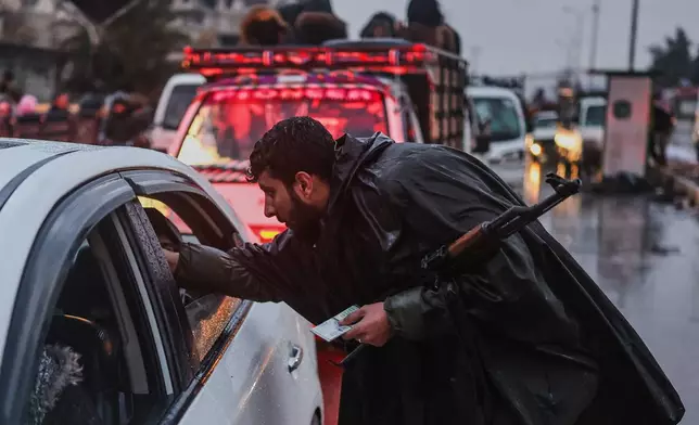 A Syrian forces officer checks the IDs of residents fleeing the Sheikh Maqsoud neighborhood of Aleppo, Syria, Friday, Jan. 9, 2026, after the government declared the area a closed military zone following days of clashes between government forces and Kurdish fighters. (AP Photo/Ghaith Alsayed)