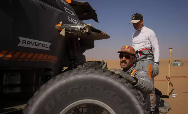 Driver Guillaume de Mevius and co-driver Mathieu Baumel change a tire of their car at the end of the ninth stage of the Dakar Rally between Wadi Ad Dawasir and Bisha, Saudi Arabia, Tuesday, Jan.13, 2026. (AP Photo/Thibault Camus)