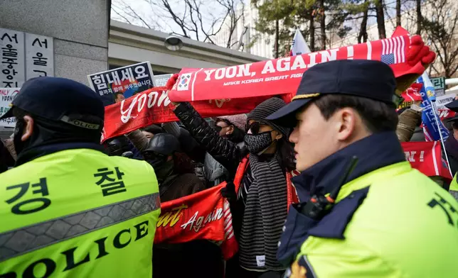Supporters of former South Korean President Yoon Suk Yeol hold signs as police officers stand guard outside Seoul Central District Court, in Seoul, South Korea, Friday, Jan. 16, 2026. (AP Photo/Lee Jin-man)