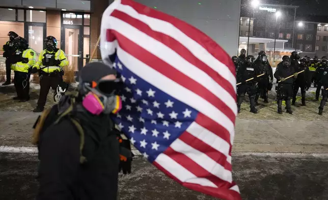 A demonstrator holds an upside-down American flag as law enforcement stand during a protest outside SpringHill Suites and Residence Inn by Marriott hotels on Monday, Jan. 26, 2026, in Maple Grove, Minn. (AP Photo/Adam Gray)