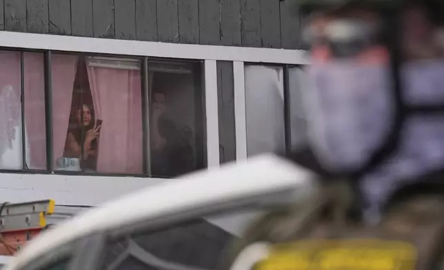 People glance out of their window as federal immigration agents work on the scene in Minneapolis, Sunday, Jan. 25, 2026. (AP Photo/Adam Gray)