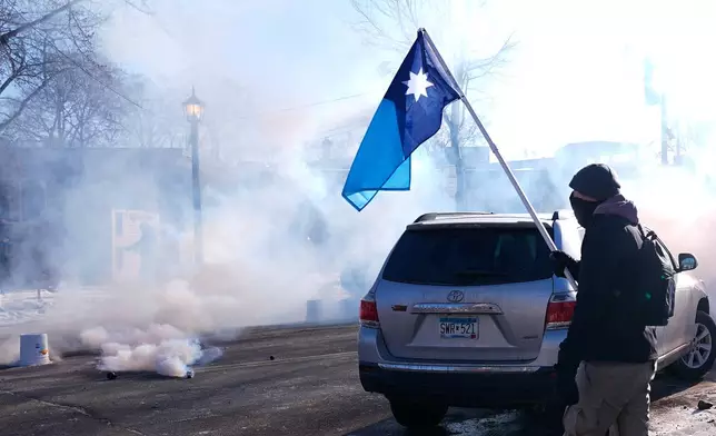 A person holds a Minnesota state flag as federal immigration officers deploy tear gas Saturday, Jan. 24, 2026, in Minneapolis. (AP Photo/Abbie Parr)