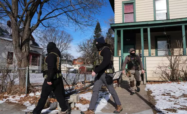 Federal immigration officers walk away after knocking on a door Monday, Jan. 26, 2026, in St. Paul, Minn. (AP Photo/Adam Gray)