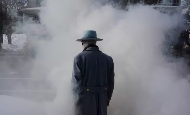 A man walks into smoke from tear gas dispersed by federal agents, during a protest, Monday, Jan. 12, 2026 in Minneapolis (AP Photo/Adam Gray)