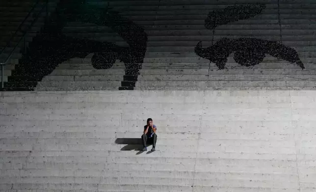 A man sits on steps decorated with a mural representing the eyes of late Venezuelan President Hugo Chavez in Caracas, Venezuela, Monday, Jan. 12, 2026. (AP Photo/Matias Delacroix)