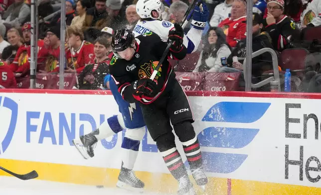 Chicago Blackhawks center Oliver Moore (11) and Tampa Bay Lightning defenseman Max Crozier (24) crash against the boards during the second period of an NHL hockey game Friday, Jan. 23, 2026, in Chicago. (AP Photo/Erin Hooley)