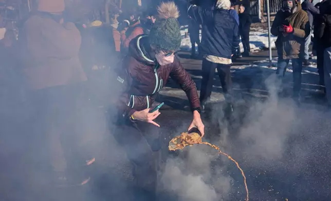 A protester grabs a tear gas grenade deployed by federal immigration officers near the scene where Renee Good was fatally shot by an ICE officer last week, Tuesday, Jan. 13, 2026, in Minneapolis. (AP Photo/John Locher)