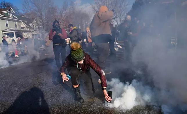 A protester grabs a tear gas grenade deployed by federal immigration officers near the scene where Renee Good was fatally shot by an ICE officer last week, Tuesday, Jan. 13, 2026, in Minneapolis. (AP Photo/John Locher)