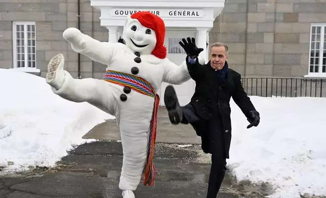 Prime Minister Mark Carney, right, and Bonhomme Carnaval raise their legs together in a traditional carnival kick, at the beginning of a Cabinet planning forum at the Citadelle in Quebec City, Thursday, Jan. 22, 2026.(Jacques Boissinot /The Canadian Press via AP)