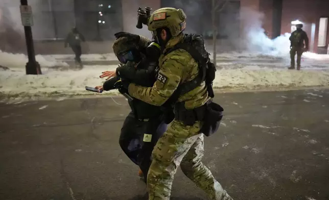 A federal agent holds a person as the agents try to clear the demonstrators near a hotel, using tear gas during a noise demonstration protest in response to federal immigration enforcement operations in the city Sunday, Jan. 25, 2026, in Minneapolis. (AP Photo/Adam Gray)