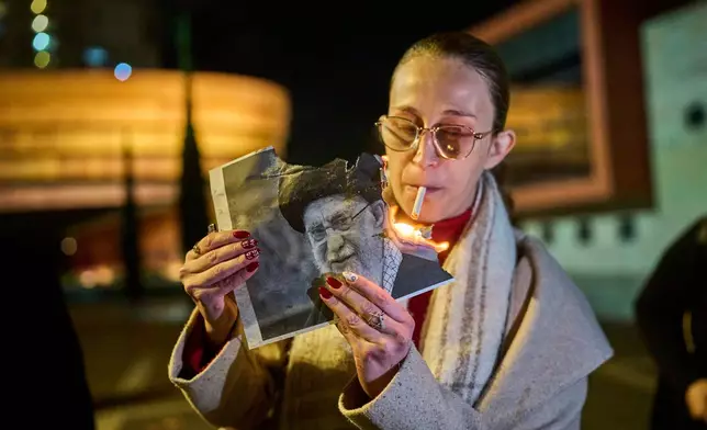 A demonstrator lights a cigarette with a burning poster depicting Supreme Leader Ayatollah Ali Khamenei during a rally in support of Iran's anti-government protests, in Holon, Israel, Wednesday, Jan. 14, 2026. (AP Photo/Ohad Zwigenberg)