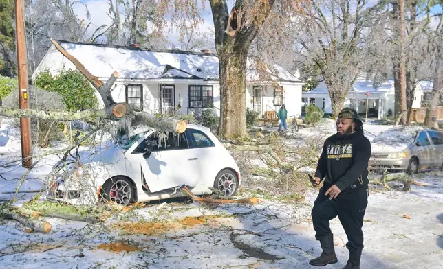 A man walks past a car damaged by a tree that fell during an ice storm, in Oxford, Miss. on Monday, Jan. 26, 2026. (AP Photo/Bruce Newman)