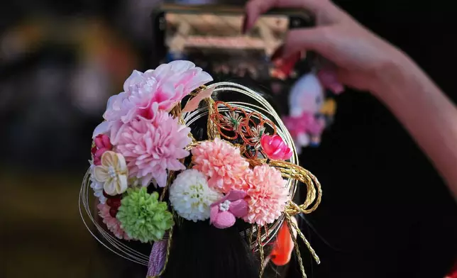 A young adult with hair ornament takes a photo, during a ceremony of the Coming-of-Age Day, a centuries-old tradition and national holiday marking the milestone from childhood to adulthood, Monday, Jan. 12, 2026, in Yokohama near Tokyo. (AP Photo/Eugene Hoshiko)