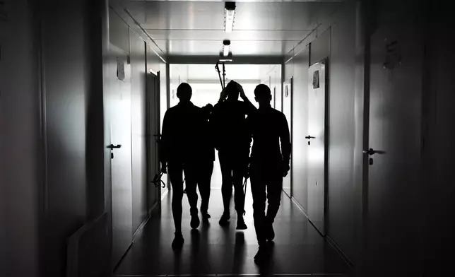 Biathletes Yekateryna Mashtalier, 18, Mykola Dorofeiev, 16, Maksym Kravchenko, 17, and Nazar Kravchenko, 12, walk through a dark hallway during a blackout at their mobile gym outside the destroyed ski base in Chernihiv, Ukraine, Thursday, Oct. 30, 2025. (AP Photo/Julia Demaree Nikhinson)