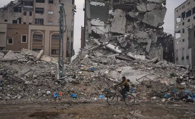 A Palestinian man rides a bicycle past destroyed buildings in Gaza City Sunday, Jan. 4, 2026. (AP Photo/Jehad Alshrafi)