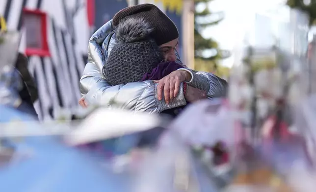 People mourn behind flowers and letters near the sealed off Le Constellation bar, where a devastating fire left dead and injured during the New Year's celebrations in Crans-Montana, Swiss Alps, Switzerland, Friday, Jan. 2, 2026. (AP Photo/ Antonio Calanni)