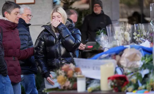 People bring flowers near the sealed off Le Constellation bar, where a devastating fire left dead and injured during the New Year's celebrations in Crans-Montana, Swiss Alps, Switzerland, Friday, Jan. 2, 2026. (AP Photo/ Antonio Calanni)