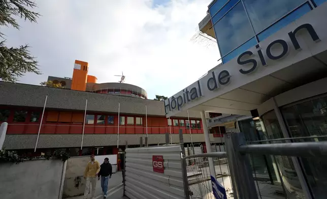 Two men walk outside a hospital as a helicopter takes off in Sion, Switzerland, Friday, Jan. 2, 2026, following the fire at the "Le Constellation" bar and lounge in Crans-Montana, Switzerland during the New Year celebration. (AP Photo/Baz Ratner)