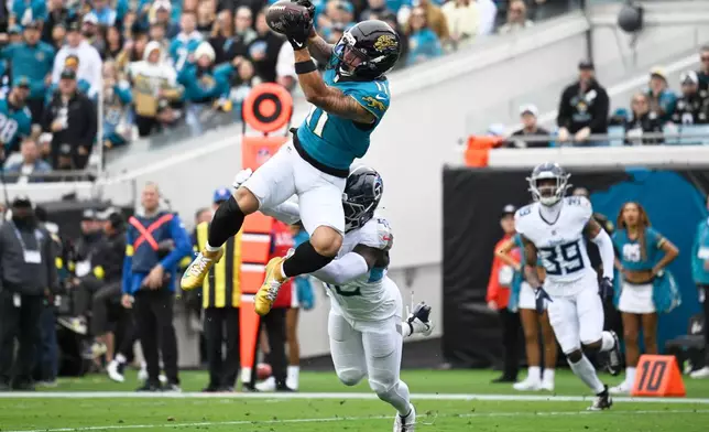 Jacksonville Jaguars wide receiver Parker Washington (11) makes a catch for a touchdown over Tennessee Titans safety Sanoussi Kane, below, during the first half of an NFL football game Sunday, Jan. 4, 2026, in Jacksonville, Fla. (AP Photo/Phelan M. Ebenhack)