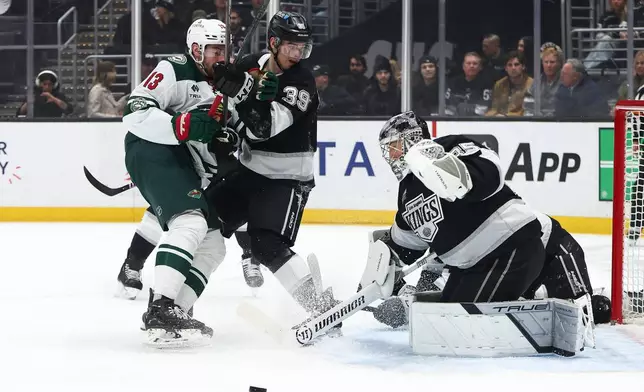 Los Angeles Kings goaltender Darcy Kuemper, right, makes a save as Minnesota Wild center Yakov Trenin (13) and Kings left wing Jeff Malott (39) watch during the first period of an NHL hockey game, Monday, Jan. 5, 2026, in Los Angeles. (AP Photo/Jessie Alcheh)