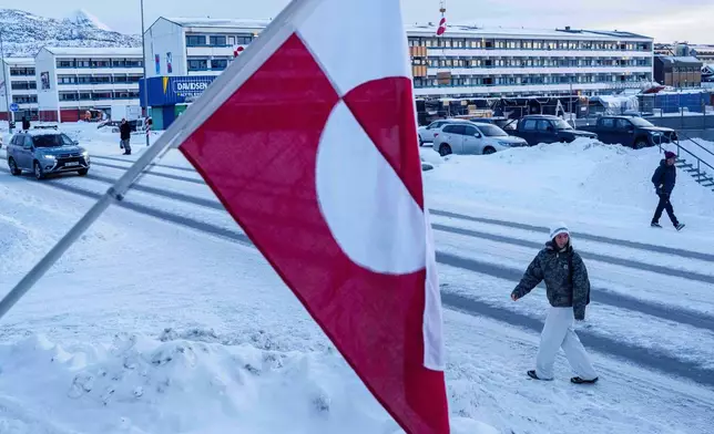 A woman walks on a street past a Greenlandic national flag in Nuuk, Greenland, Wednesday, Jan. 14, 2026. (AP Photo/Evgeniy Maloletka)