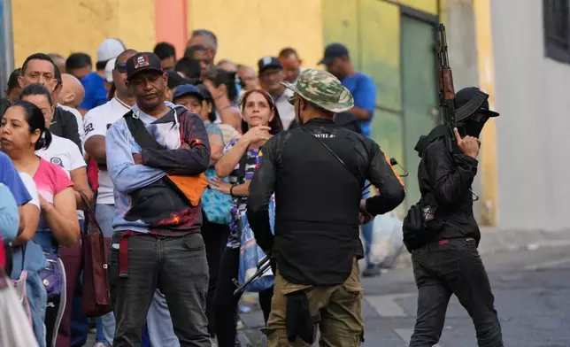 Pro-government armed civilians monitor shoppers lining up outside a supermarket in Caracas, Venezuela, Sunday, Jan. 4, 2026.(AP Photo/Ariana Cubillos)
