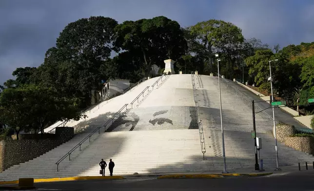 Pedestrians stand in a square decorated with images of the eyes of former President Hugo Chavez in Caracas, Venezuela, Sunday, Jan. 4, 2026. (AP Photo/Ariana Cubillos)