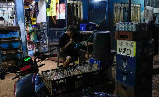 A man sucks on a water hose to fill bottles with gasoline to sell in the gold mining region of El Callao, Venezuela, Tuesday, Jan. 22, 2026. (AP Photo/Matias Delacroix)