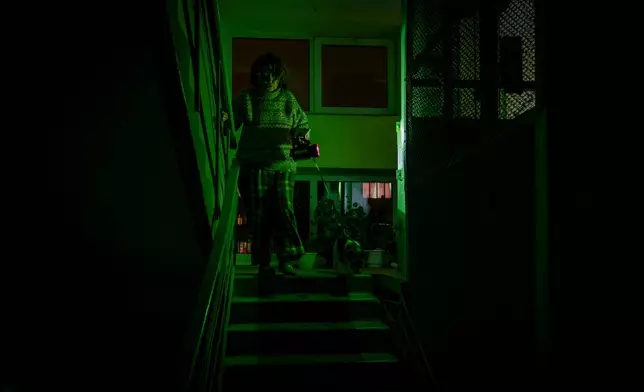 Tetiana Tatarenkova shines a flashlight as she goes to see her neighbour during a blackout caused by Russia's regular air attacks against the country's energy infrastructure in Kyiv, Ukraine, Tuesday, Jan. 13, 2026. (AP Photo/Dan Bashakov)