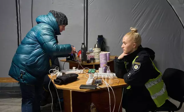 A woman charges her phone in one of the tents set up by the emergency service following Russia's regular air attacks against the country's energy objects, that leave residents without power, water and heating in the dead of winter, in Kyiv, Ukraine, Tuesday, Jan. 13, 2026. (AP Photo/Efrem Lukatsky)