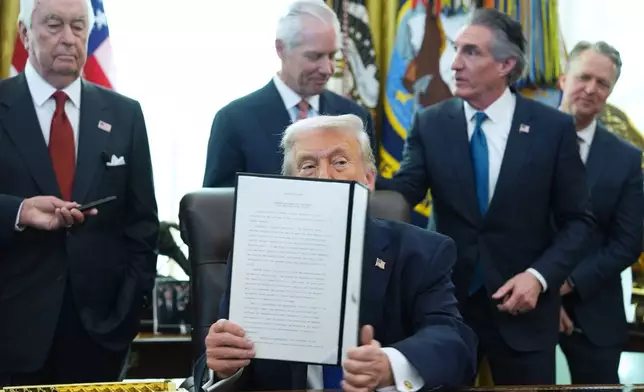 President Donald Trump holds an executive order he signed in the Oval Office of the White House, Friday, Jan. 30, 2026, in Washington. (AP Photo/Evan Vucci)