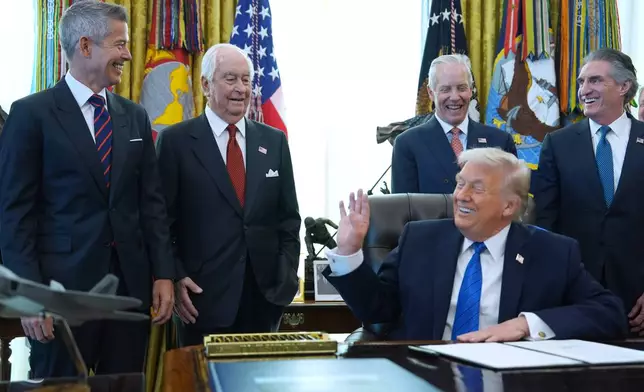 President Donald Trump speaks to Roger Penske, second left. as he signs executive orders in the Oval Office of the White House, Friday, Jan. 30, 2026, in Washington. (AP Photo/Evan Vucci)