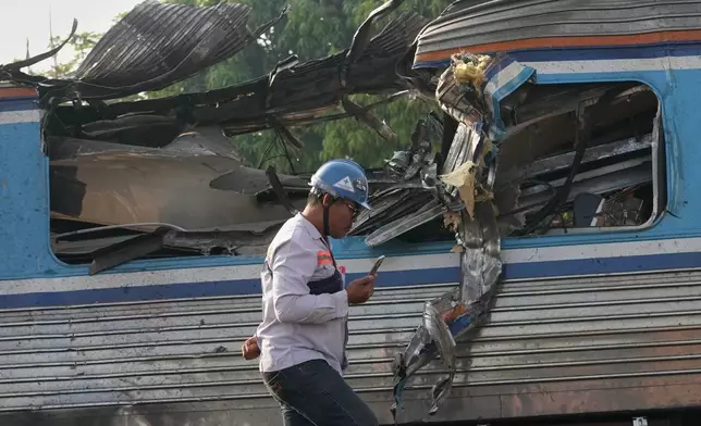 A train worker walks in front of the wreckage of train, a day after a construction crane fell into a passenger train in Nakhon Ratchasima province, Thailand, Thursday, Jan. 15, 2026. (AP Photo/Sakchai Lalit)