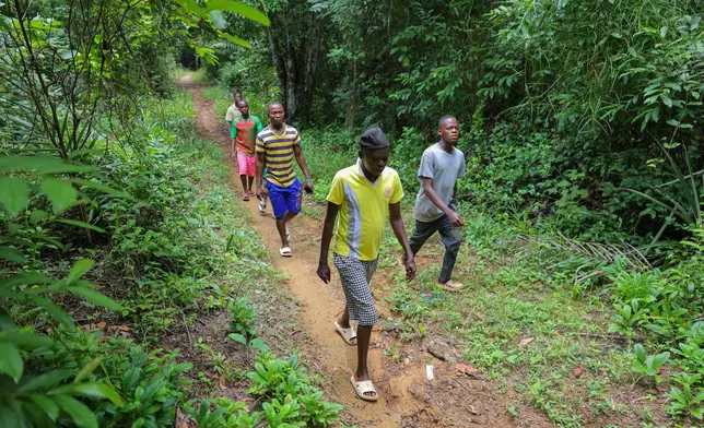 Mustapha Pabai, the town chief, front, walks with residents along a narrow path leading to the river, which was poisoned by mining waste, in Jikando, Liberia, July 8, 2025. (AP Photo/Misper Apawu)
