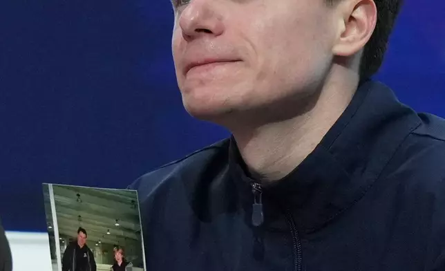 Maxim Naumov holds a photo of his parents while he waits for his scores after competing during the men's short program at the U.S. Figure Skating Championships, Thursday, Jan. 8, 2026, in St. Louis. Naumov's parents were killed in a plane crash in early 2025. (AP Photo/Stephanie Scarbrough)