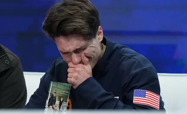 Maxim Naumov holds a photo of his parents while he waits for his scores after competing during the men's short program at the U.S. Figure Skating Championships, Thursday, Jan. 8, 2026, in St. Louis. Naumov's parents were killed in a plane crash in early 2025. (AP Photo/Stephanie Scarbrough)