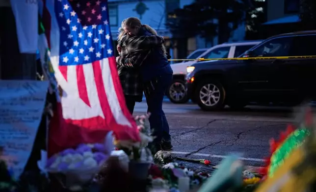 Monica Travis shares an embrace while visiting a makeshift memorial for Renee Good, who was fatally shot by an ICE officer last week, Monday, Jan. 12, 2026, in Minneapolis. (AP Photo/John Locher)